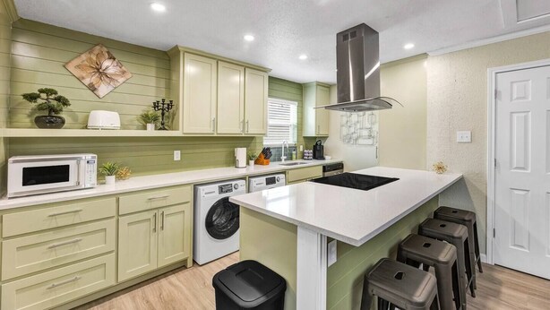 A compact kitchen with a microwave, washing machine, and a stove.