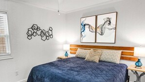 A bedroom with a large bed, a wooden headboard, two wall-mounted artworks, and a geometric wall decoration.