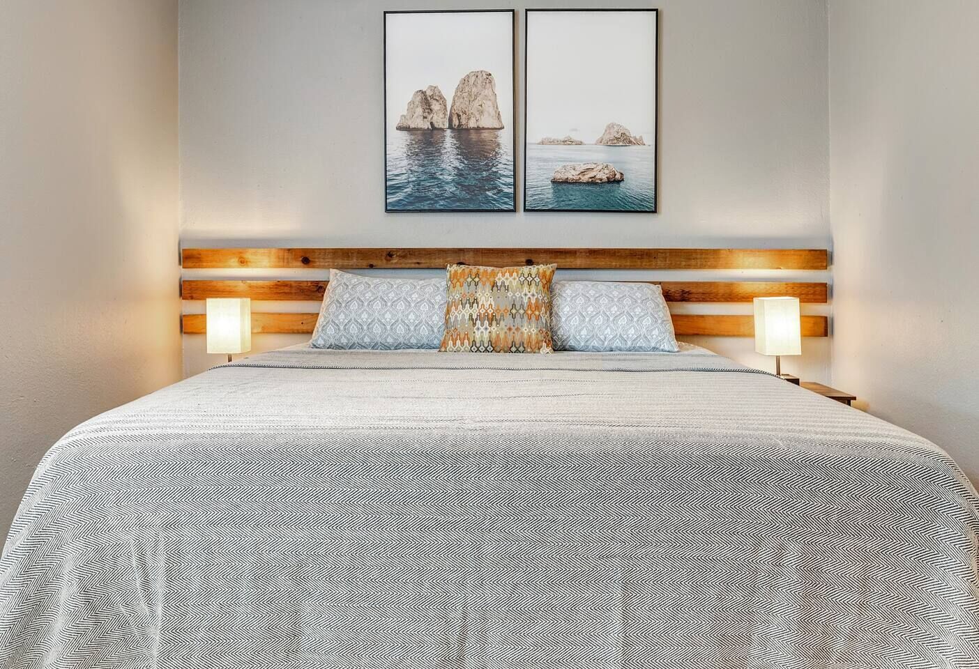 Un lit bien fait, avec une couvre-lit à motifs, une tête de lit en bois et deux lampes fixées au mur.