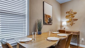 A dining area with a wooden table set for four, flanked by leather chairs. A potted plant and a framed picture adorn the wall. - Kelly's Cove: 1st Flr 2 Bdrm-Walk to A&M-King Beds (Bryan)