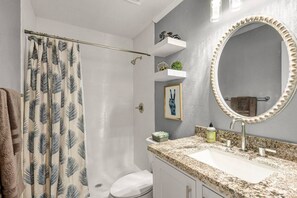 Bathroom features a shower area with a leaf-patterned curtain, a toilet, sink, and large mirror.