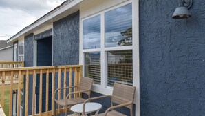 A covered outdoor area with a wooden deck, wicker chairs, and a large window with blinds. - Magnolia Farms: Walk to A&M, Comfy King Beds (Bryan)