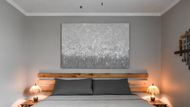 A bedroom with a bed, two bedside lamps, a wooden headboard, and a large abstract painting on the wall. - Magnolia Farms: Walk to A&M, Comfy King Beds (Bryan)
