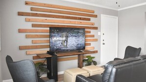 A modern living room with a flat-screen TV mounted on a wooden slat wall, leather sofas, and a small coffee table. - Magnolia Farms: Walk to A&M, Comfy King Beds (Bryan)