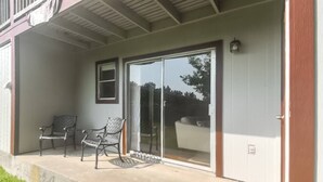 Une terrasse couverte avec deux chaises et une porte-fenêtre coulissante donnant sur un jardin.