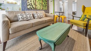 Un salon avec un canapé beige, des coussins à motifs, une table basse verte et un fauteuil jaune.