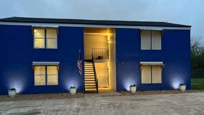 Un bâtiment bleu avec une entrée centrale, un drapeau et un escalier menant à un étage supérieur.