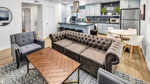 Un salon moderne avec un canapé gris, une table basse en bois et un coin repas comprenant une table et des chaises blanches.