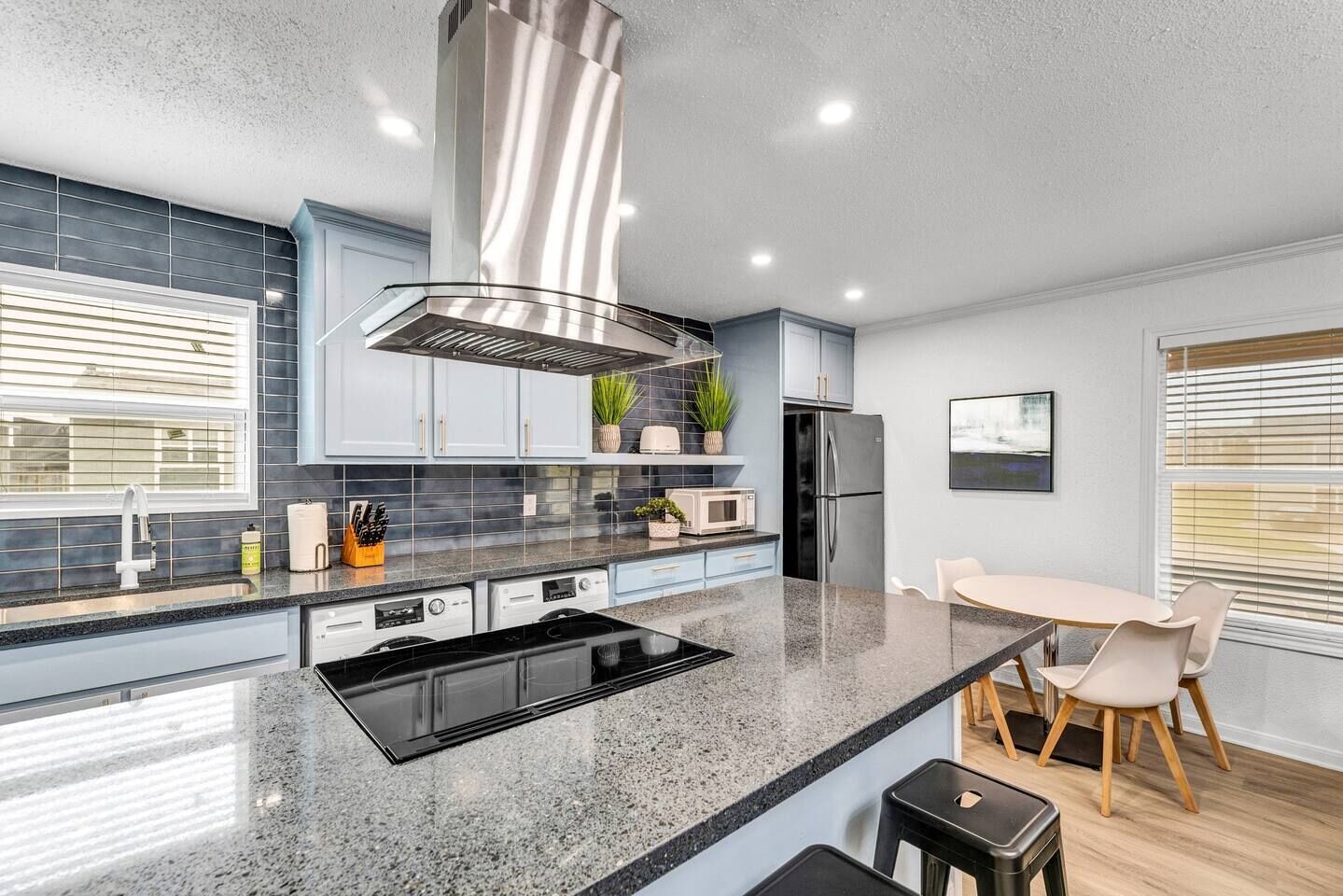 Cozinha moderna com ilha central, eletrodomésticos de aço inoxidável e área de jantar com mesa e cadeiras.