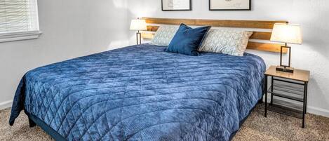 A bedroom with a large bed, two bedside tables with lamps, and two framed certificates on the wall.