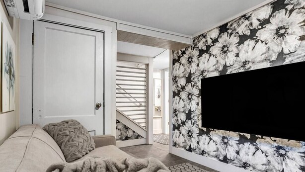 A modern living room with a sofa, a large TV, and a floral wallpaper. - Poppy: Quirky, Walk to A&M, Comfy King Bed, Fun Space (Bryan)
