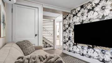 A modern living room with a sofa, a large TV, and a floral wallpaper.