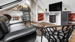 A modern loft-style living space with a sofa, chairs, a TV, and a staircase leading to an upper level. - Poppy: Quirky, Walk to A&M, Comfy King Bed, Fun Space (Bryan)