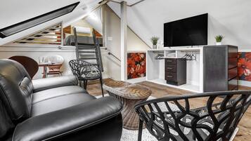 A modern loft-style living space with a sofa, chairs, a TV, and a staircase leading to an upper level.