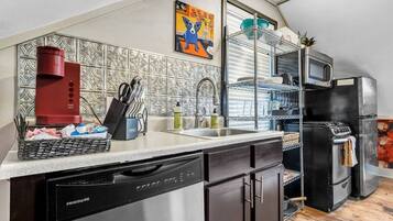 A compact kitchen with a dishwasher, a red coffee maker, and a black oven.