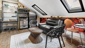 A modern kitchen with a dining area, featuring a black leather sofa, a wicker ottoman, and a dining table with chairs. - Poppy: Quirky, Walk to A&M, Comfy King Bed, Fun Space (Bryan)