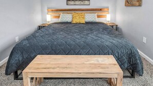 A bedroom with a large bed, a wooden headboard, a bedside table, a bench, and a wall-mounted artwork. - Rowan: 1st Floor, King Beds/Close to A&M (Bryan)