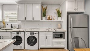 A modern kitchen with white cabinetry, a built-in washer and dryer, a stainless steel refrigerator, and a microwave. - Rowan: 1st Floor, King Beds/Close to A&M (Bryan)