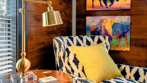 Une pièce avec un canapé à motifs, un coussin jaune, un lampadaire en laiton et deux tableaux représentant des bisons accrochés au mur.