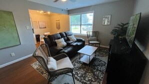 Una sala de estar con un sofá de cuero negro, una mesa de centro, un sillón negro y un mueble para televisión.