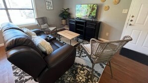 Una sala de estar con sofá, mesa de centro, sillón de mimbre, televisor y decoración mural.