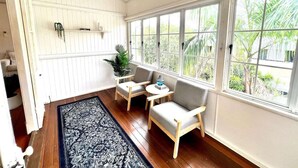 A sunroom with wooden flooring, white walls, and large windows offering a view of greenery.