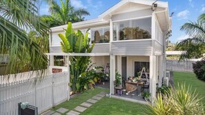 A two-story house with a covered patio, a fenced backyard, and lush greenery.