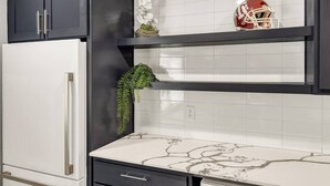 A kitchen with a white refrigerator, black cabinets, a marble countertop, and a red football helmet on a shelf. - The 12: 1st Floor 2 Bdrm, Walk to A&M, King Beds (Bryan)
