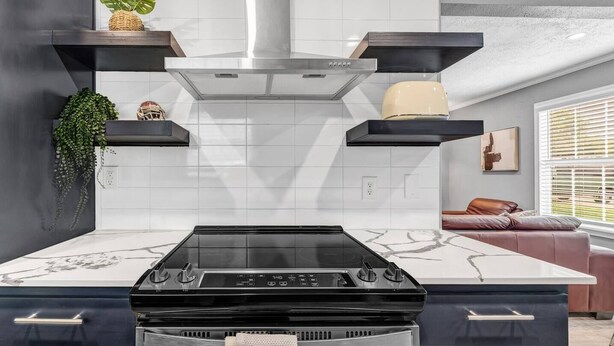A modern kitchen with a central island, black cabinetry, and a stainless steel range hood. - The 12: 1st Floor 2 Bdrm, Walk to A&M, King Beds (Bryan)