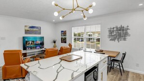 A modern kitchen with a marble island, white cabinetry, and a built-in oven. There are orange chairs and a dining table with a wooden top. - The Dominion: 2 Bdrm/Walk to A&M/Comfy King Beds (Bryan)