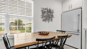 A modern kitchen with a wooden dining table, black chairs, a white refrigerator, and a geometric wall art piece. - The Dominion: 2 Bdrm/Walk to A&M/Comfy King Beds (Bryan)