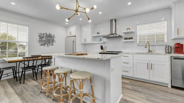 A modern kitchen with white cabinetry, a central island with stools, a stainless steel range hood, and a pendant light. - The Dominion: 2 Bdrm/Walk to A&M/Comfy King Beds (Bryan)