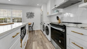 A modern kitchen with white cabinetry, a built-in oven, a dishwasher, and a large window providing natural light. - The Dominion: 2 Bdrm/Walk to A&M/Comfy King Beds (Bryan)