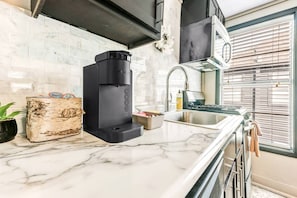 Une cuisine moderne équipée d’une machine à café intégrée, d’un évier et d’une fenêtre avec des stores.