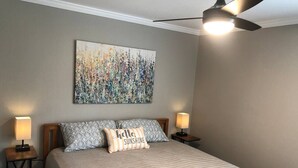 A bedroom with a bed, two bedside lamps, a ceiling fan, and a large abstract painting on the wall. - Wildflower: Very Near Texas A&M-Comfy King Beds (Bryan)