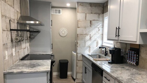A compact kitchen with white cabinets, a stainless steel range hood, a built-in oven, and a coffee maker. - Wildflower: Very Near Texas A&M-Comfy King Beds (Bryan)