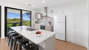Een moderne keuken met een groot eiland, witte kasten, een roestvrijstalen afzuigkap en uitzicht op groen.