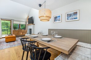 Uma área de refeições com uma mesa de madeira posta para quatro pessoas, cadeiras pretas e uma luminária pendente de fibra natural.