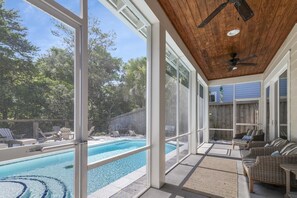 A poolside area with a clear view of the pool, wicker furniture, and a ceiling fan.