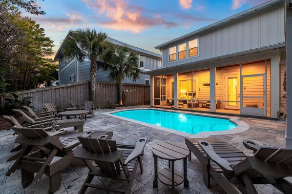 A backyard with a swimming pool, outdoor furniture, and a covered patio area.