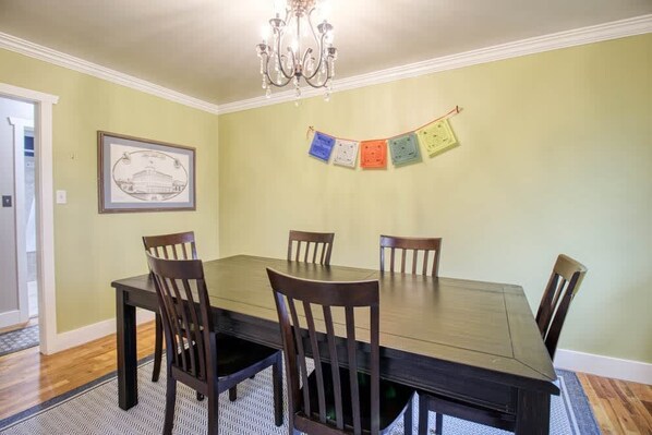 A dining room with a large table and six chairs, a chandelier, and a banner on the wall. - 4BR Charm - Fenced In - Near Harrison Ave, Pets OK (Leadville)