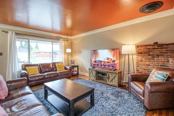 A living room with a brown leather sofa, a coffee table, and a TV on a wooden stand. - 4BR Charm - Fenced In - Near Harrison Ave, Pets OK (Leadville)