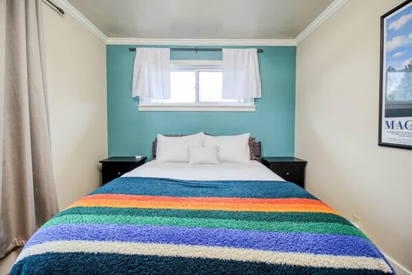 Un dormitorio con una cama, cortinas blancas, una ventana y un cuadro en la pared.