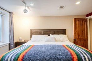 Un dormitori amb llit, una tauleta de nit, una porta de fusta i una finestra amb cortines.