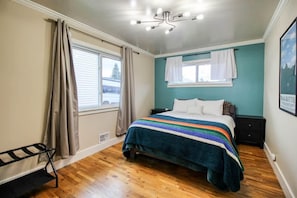 A bedroom with a bed, a bench, a window with curtains, and a ceiling light fixture.