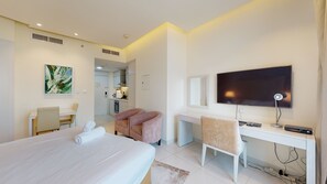 A hotel room with a bed, a desk, a chair, a TV, and a bathroom visible through an open door.
