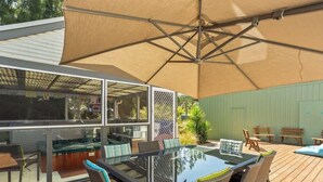 Ein möblierter Patio mit Glastisch, Stühlen und einem großen Sonnenschirm.