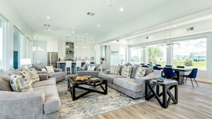 A spacious living room with a large gray sectional sofa, a coffee table, and a dining area with blue chairs. - Beachfront Beauty w/ 5 Decks, Private Walkover, Spacious Living Area & Elevator! (Galveston)