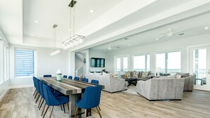 A spacious living area with a large dining table, blue chairs, and a grey sofa set. - Beachfront Beauty w/ 5 Decks, Private Walkover, Spacious Living Area & Elevator! (Galveston)