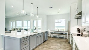 A modern kitchen with a large island, white cabinetry, and pendant lighting. - Beachfront Beauty w/ 5 Decks, Private Walkover, Spacious Living Area & Elevator! (Galveston)
